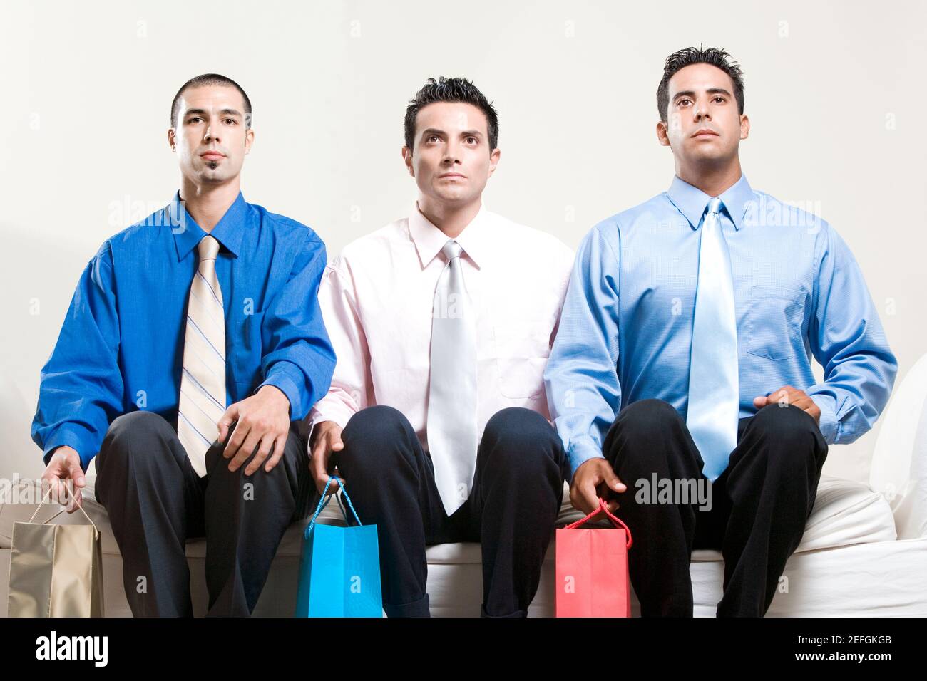 Zwei junge Männer und ein mittelalter Mann sitzen darauf Eine Couch mit Einkaufstaschen Stockfoto