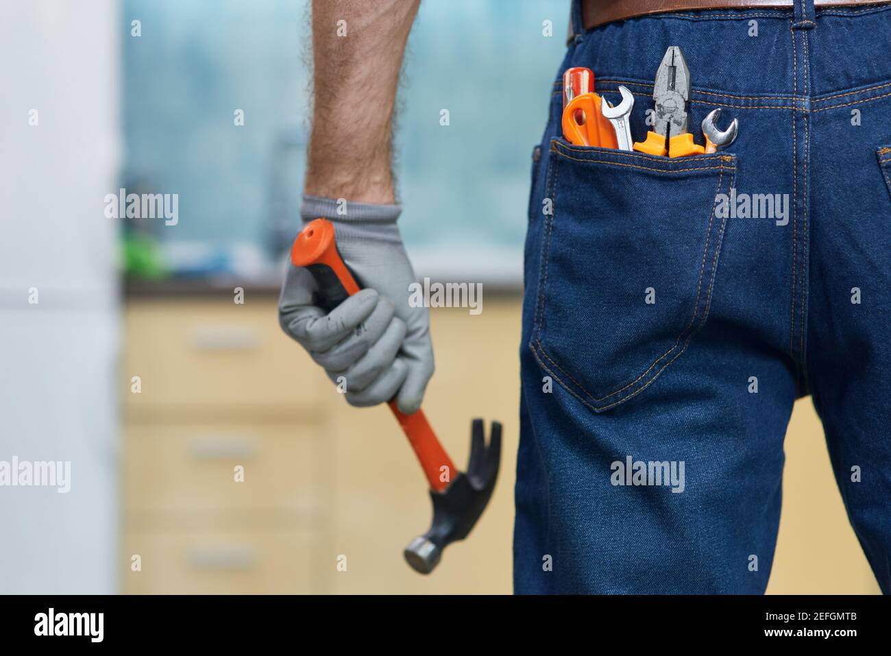 Nagel es an. Nahaufnahme von verschiedenen Sanitär-Handwerkzeuge in der Jeans Gesäßtasche des Mannes. Professionelle Werkstatt mit einem Hammer, im Innenbereich stehend Stockfoto