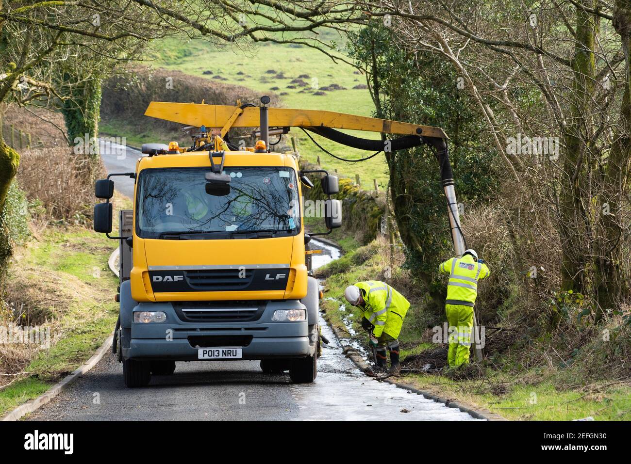 Zwei Mitarbeiter des Landkreises Lancashire, die Abflüsse auf einer Landstraße abräumen: Chipping, Preston, Lancashire. Stockfoto