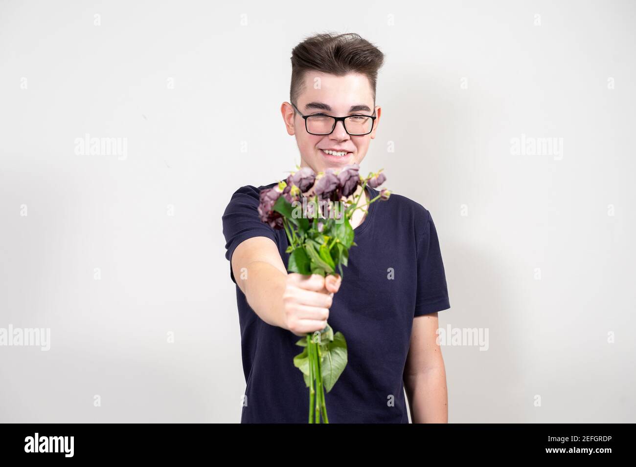 Ein junger Mann mit Brille hält einen Blumenstrauß aus verwelkelten Blumen und lächelt. Das Konzept von Gier und Geiz Stockfoto