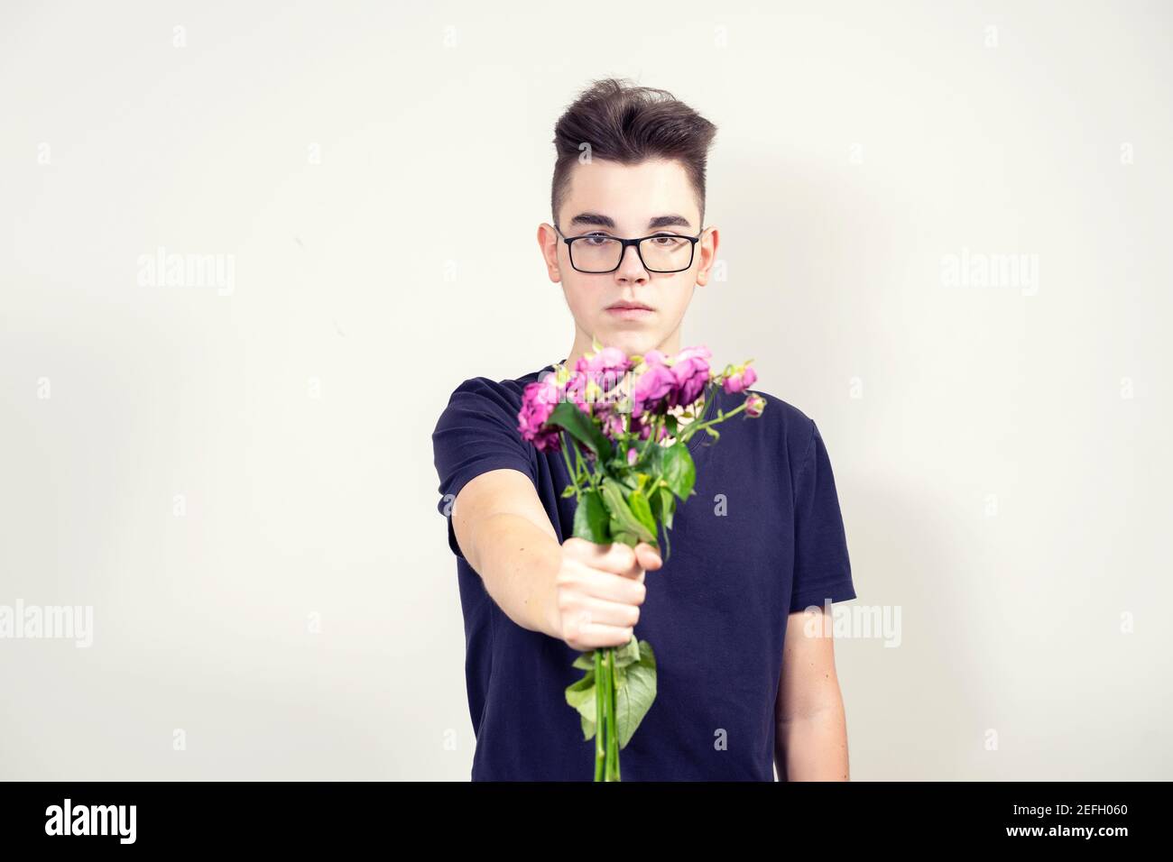 Ein ernsthafter junger Mann in Gläsern hält einen Strauß nicht frischer Blumen aus. Trennungskonzept Stockfoto