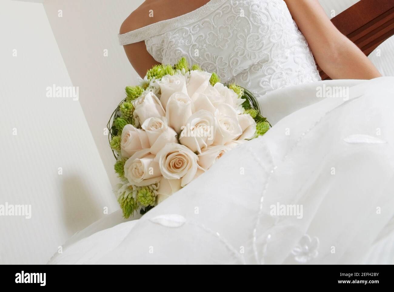 Mittelansicht einer Braut, die auf dem Bett liegt Und hält einen Blumenstrauß Stockfoto