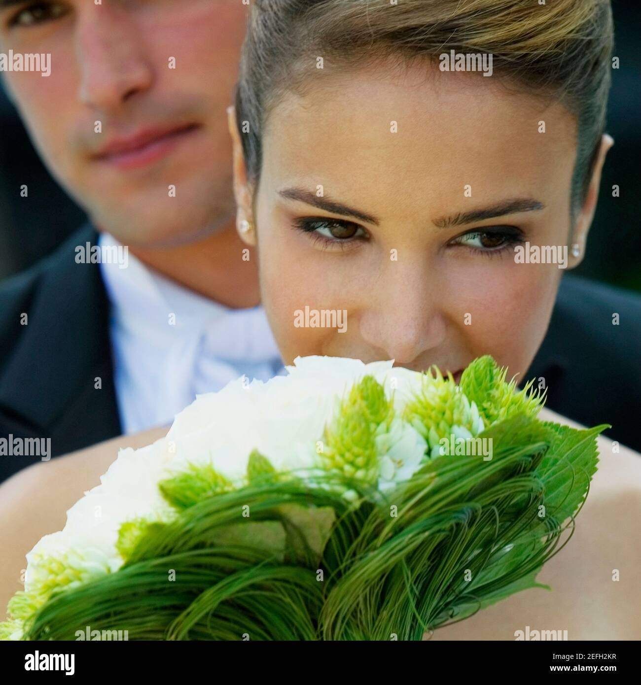 Nahaufnahme einer Braut mit einem Blumenstrauß Ihr Bräutigam im Hintergrund Stockfoto