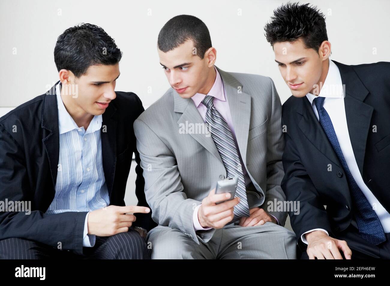 Nahaufnahme von drei Geschäftsleuten, die sitzen und ein Handy betrachten Telefon Stockfoto