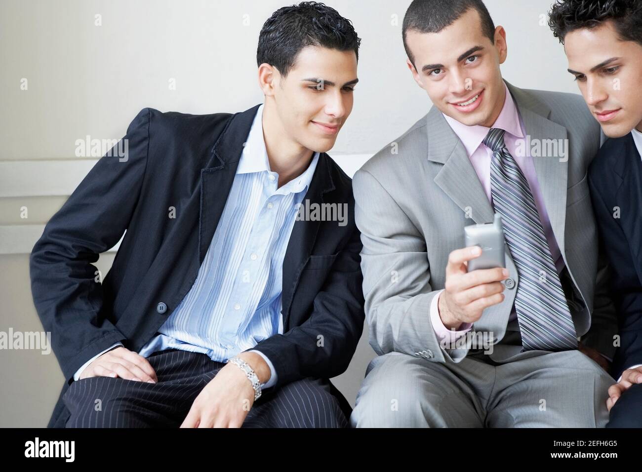 Porträt eines Geschäftsmannes mit einem Handy mit zwei Geschäftsleute, die es betrachten Stockfoto