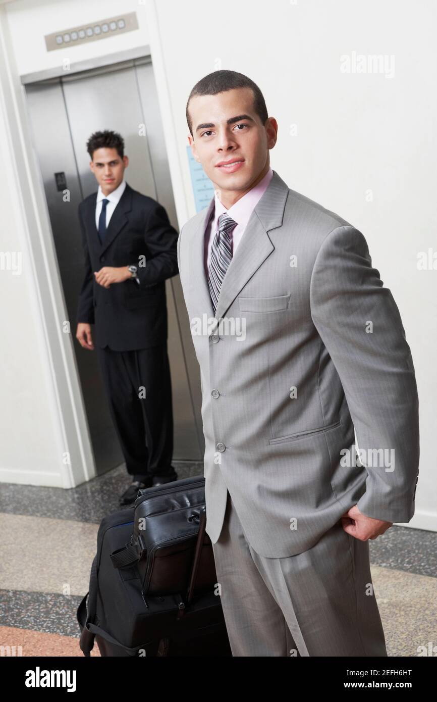 Porträt eines Geschäftsmannes mit Gepäck und eines Geschäftsmannes stehend Vor einem Aufzug Stockfoto