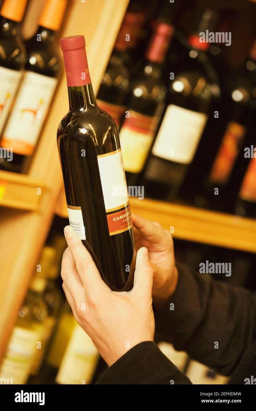 Nahaufnahme einer personŽs Hand, die eine Weinflasche in einem Spirituosenladen hält Stockfoto