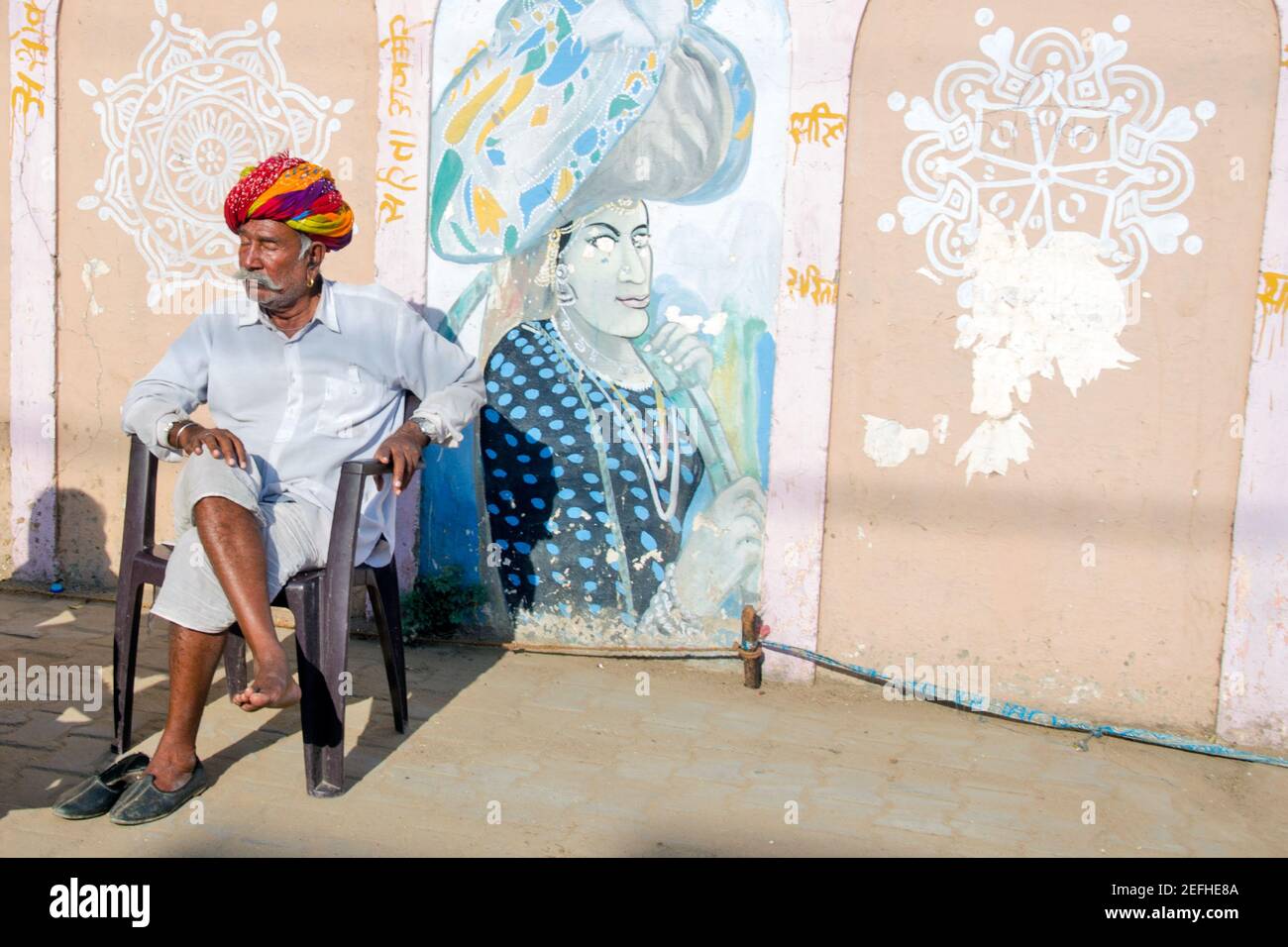 Während der Pushkar Messe, ein Kamel Handler sitzt auf dem Messegelände in der Morgensonne. Der rote Turban auf seinem Kopf ist hell und attraktiv. Stockfoto