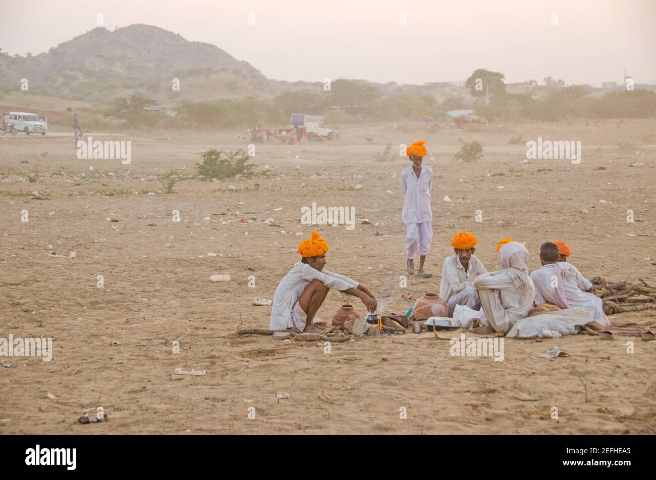 Während der Pushkar Messe sitzen eine Gruppe von Kamelhandlern auf dem Messegelände in der Abendsonne. Der orangefarbene Turban auf ihren Köpfen ist hell. Stockfoto