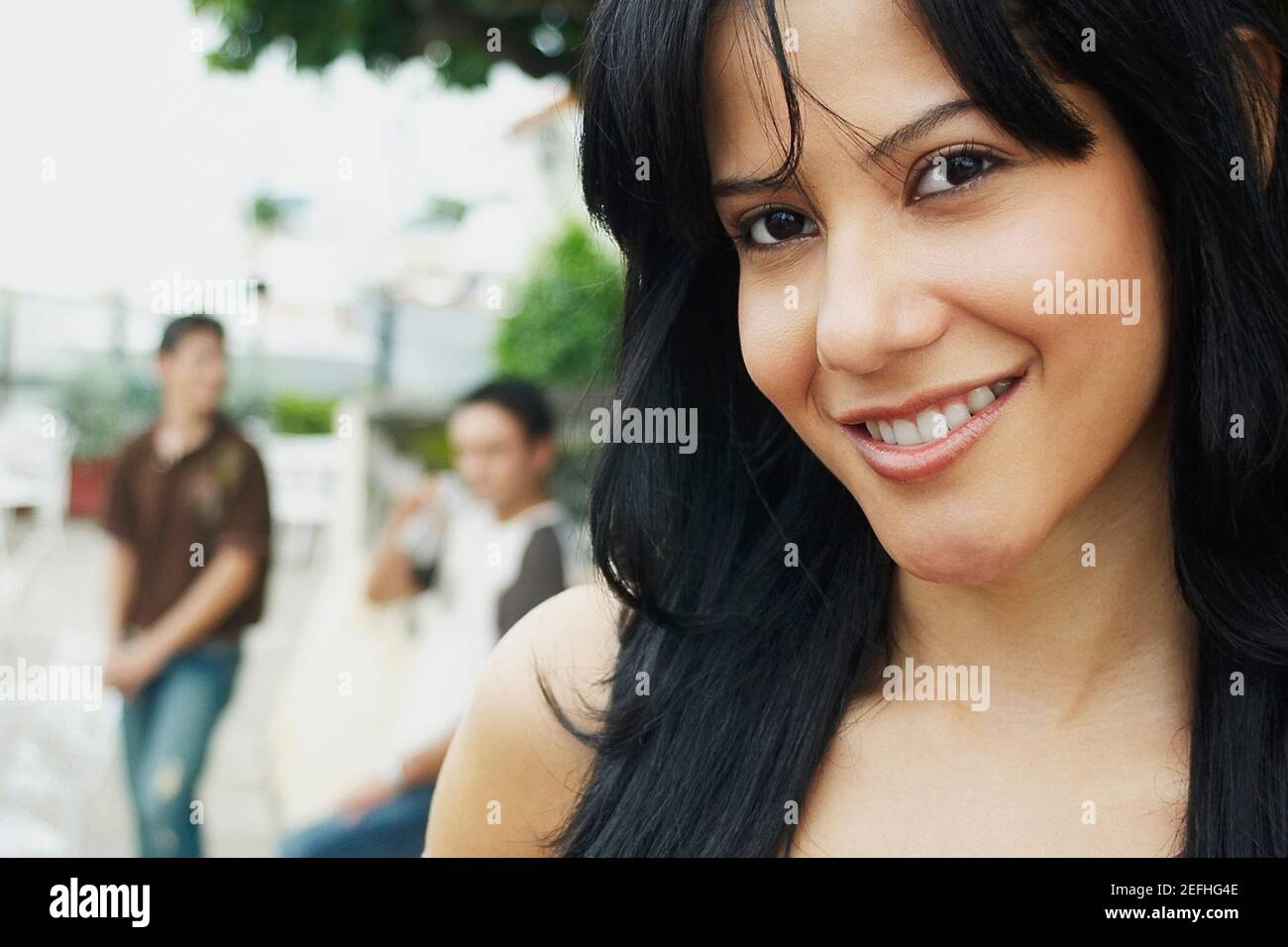 Nahaufnahme einer jungen Frau, die mit drei jungen Männern lächelt Im Hintergrund stehend Stockfoto