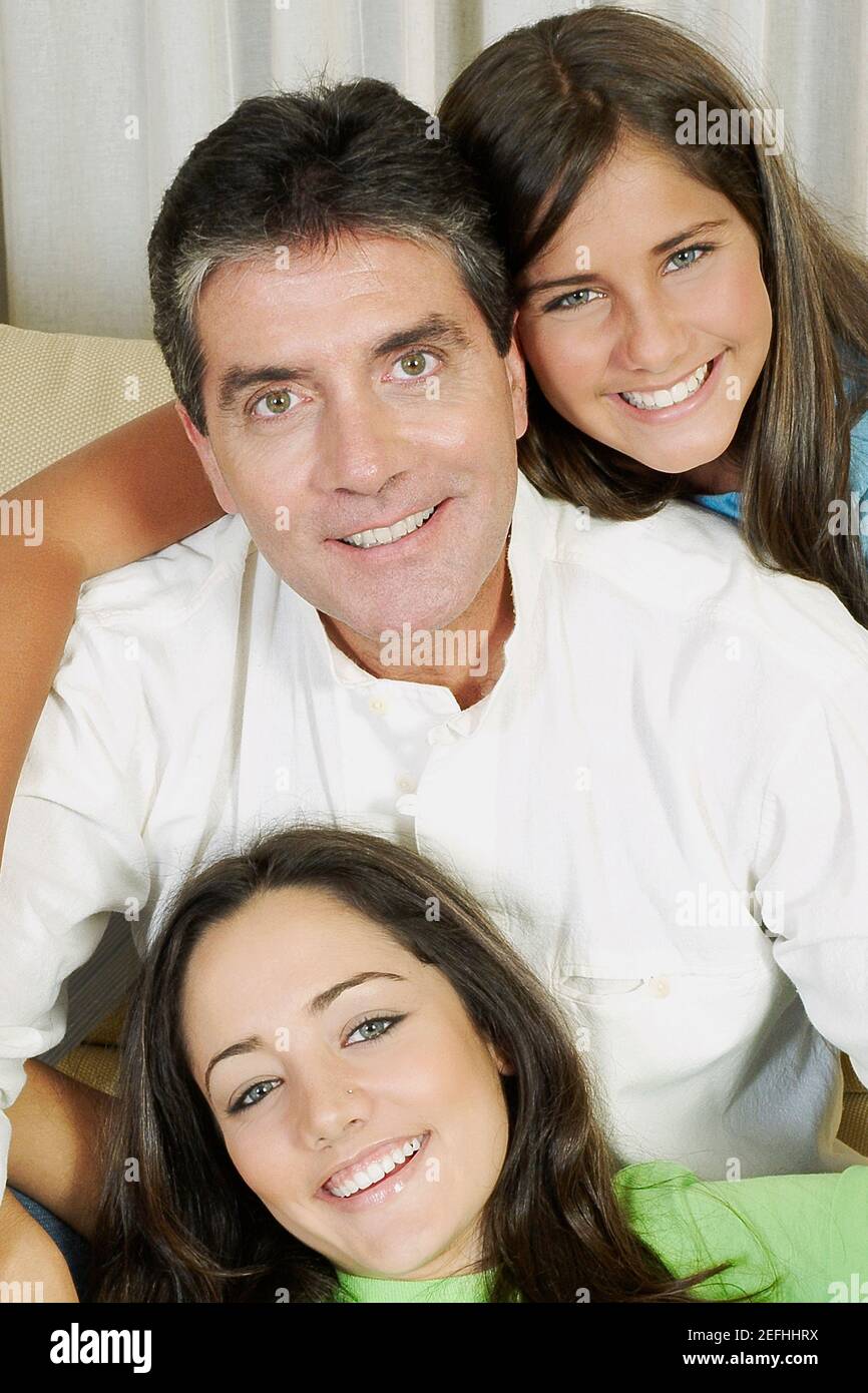Porträt eines reifen Mannes und seiner beiden Töchter im Sitzen Auf der Couch und lächelnd Stockfoto