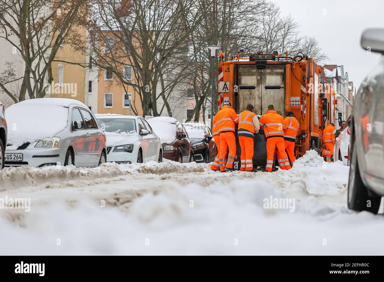 16. Februar 2021, Sachsen-Anhalt, Halle (Saale): Mitarbeiter der Stadtwerke Halle versuchen, einen Abfallcontainer durch den Tiefschnee zum Fahrzeug zu ziehen. Die Mitarbeiter der Halleschen Wasser und Stadtwirtschaft (HWS) müssen sich aufgrund der aktuellen Wetterlage mit schwierigeren Herausforderungen auseinandersetzen. In einigen Fällen müssen die vollen Abfallbehälter zwischen geparkten Autos, Schnee und Eis auf die Straßen gezogen werden. Foto: Jan Woitas/dpa-Zentralbild/ZB Stockfoto
