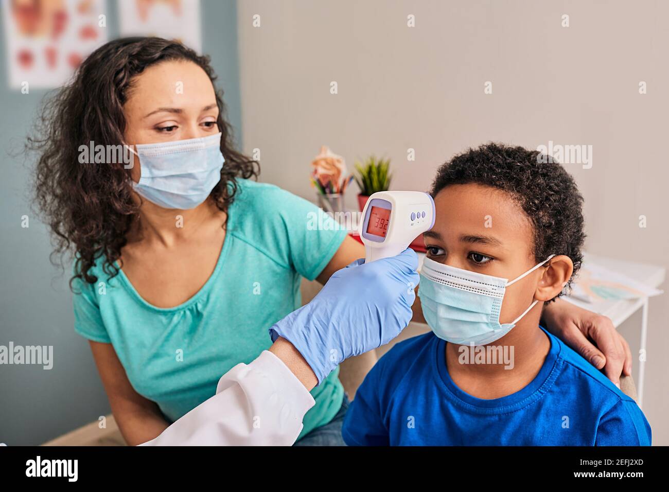 Kind trägt eine medizinische Maske während der Überprüfung seiner Körpertemperatur berührungsloses Thermometer in einer medizinischen Klinik. Afroamerikanischer Junge hat Fieber, in der Nähe Stockfoto