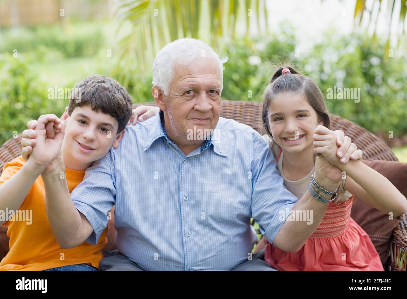 Porträt eines älteren Mannes, der seine grandchildrenÅ½s Hände hält und Lächelnd Stockfoto