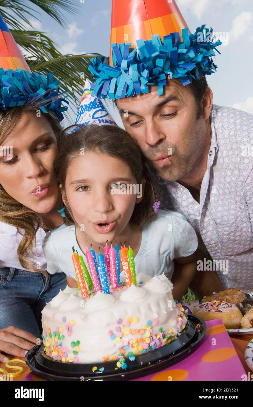 Portrait eines Mädchens mit ihren Eltern, die Kerzen aufblasen Ein Geburtstagskuchen Stockfoto