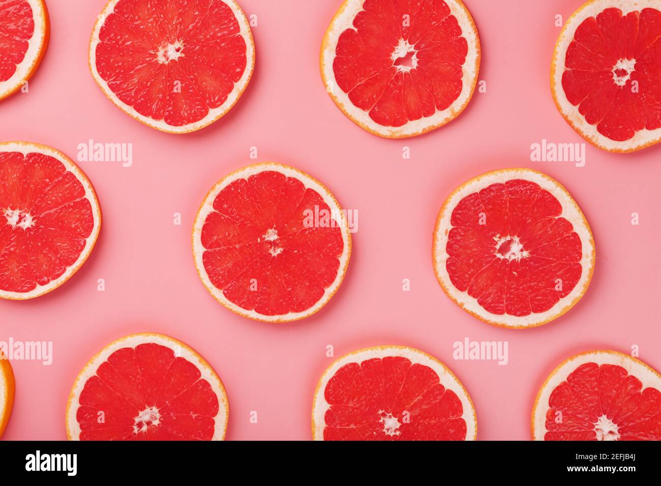 Muster von Scheiben saftiger Grapefruit auf einem rosa Hintergrund, ein schönes Muster. Draufsicht, Vollbild Stockfoto