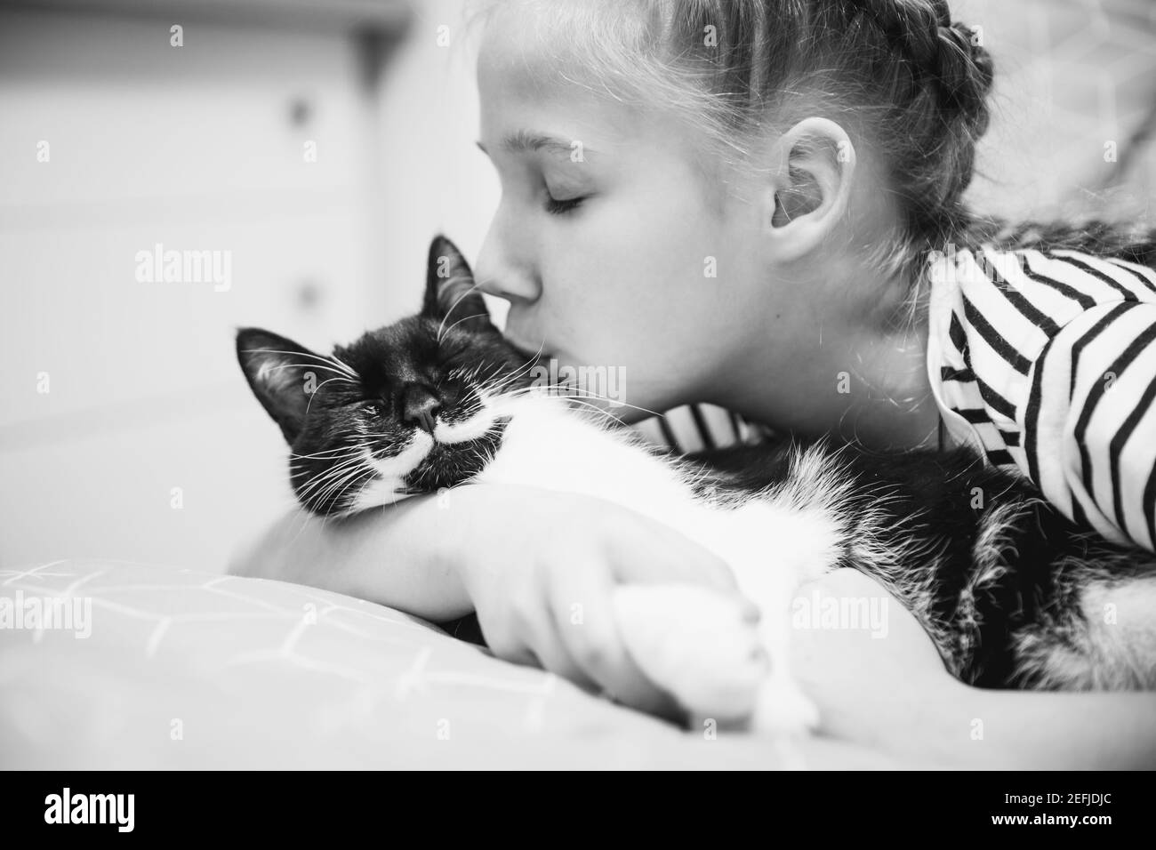 Ein Mädchen umarmt und küsst eine schwarze Katze, die ihre Augen vor Freude geschlossen hat. Stockfoto