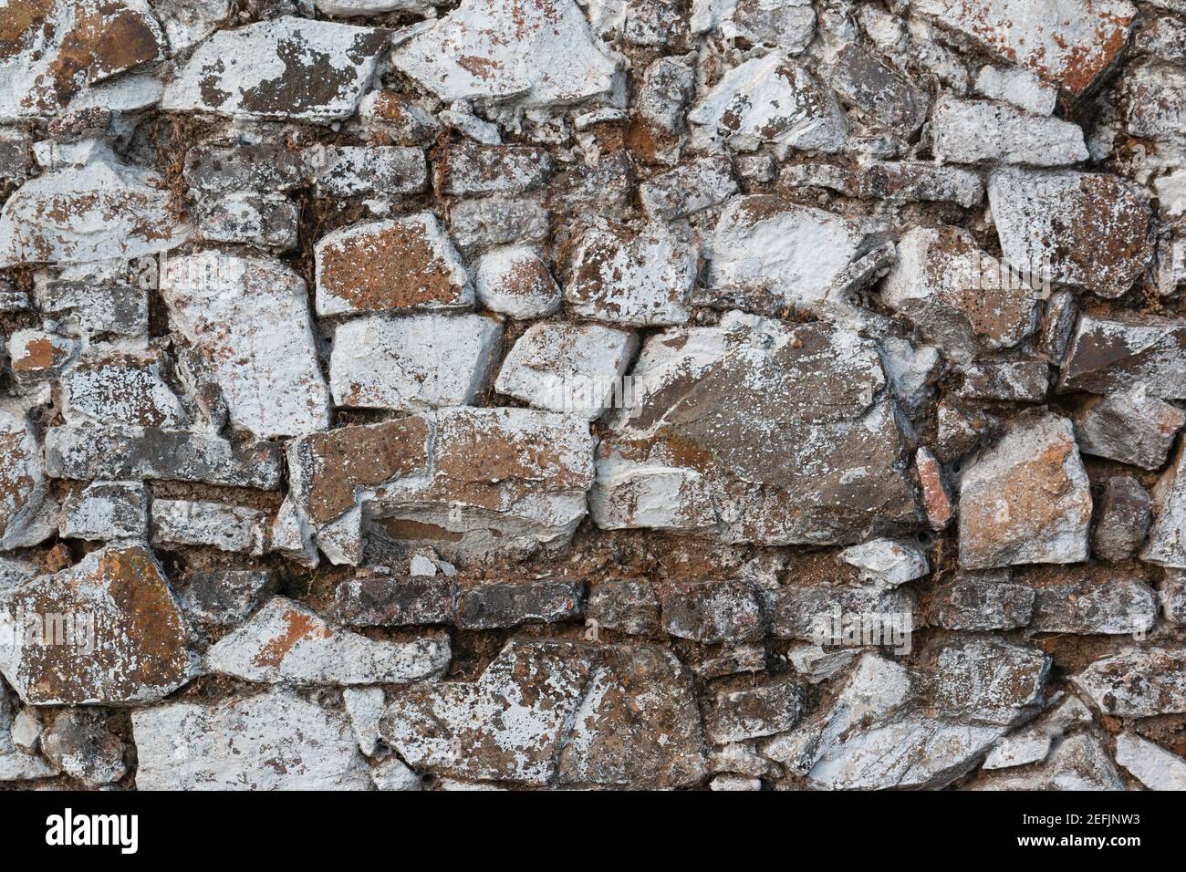 Alte Steinmauer, in einer verblassten weißen Farbe bemalt und mit Steinen und Schlamm gebaut Stockfoto