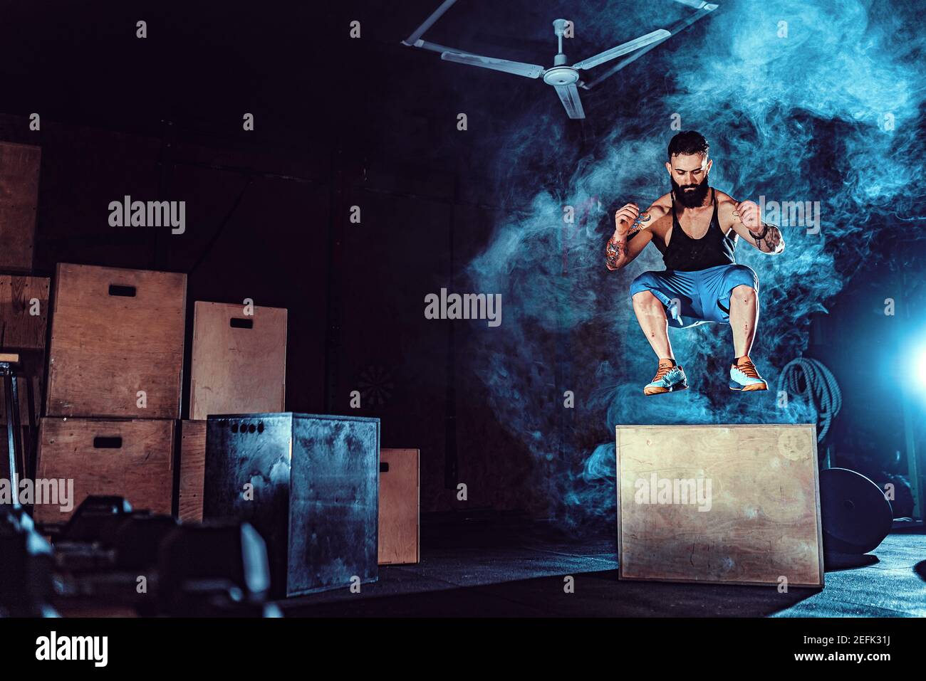 Passen tattoed bärtiger Mann springen auf ein Feld als Teil der Übung Routine. Mann tun, springen in der Turnhalle. Sportler ist die Box springt. Stockfoto