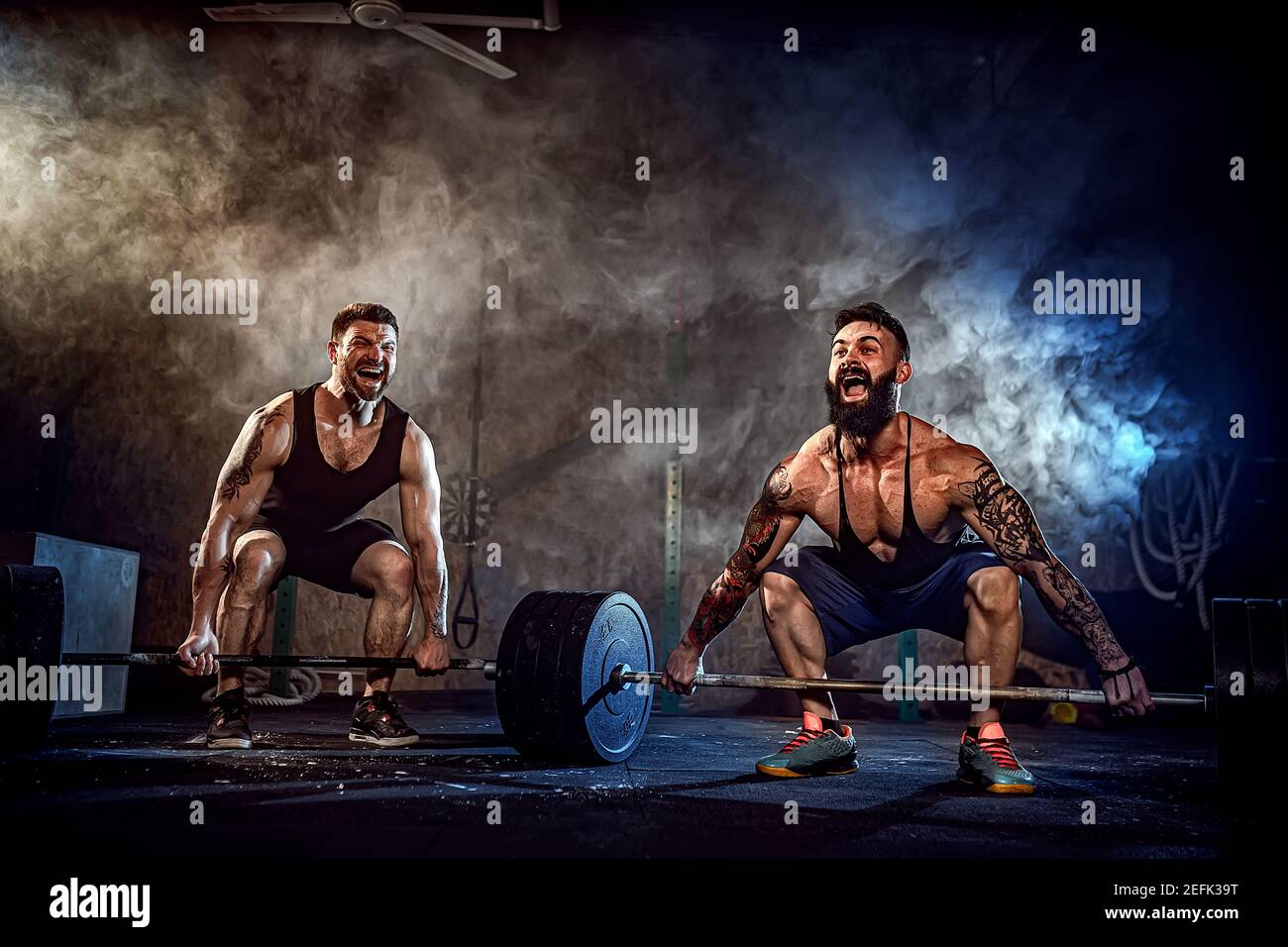 Zwei muskulösen Bärtigen tattoed Athleten training, Heben von schweren Gewicht bar in Rauch am Gym. Schreien. Hart zu arbeiten. Übung für die Muskeln der Rückseite Stockfoto