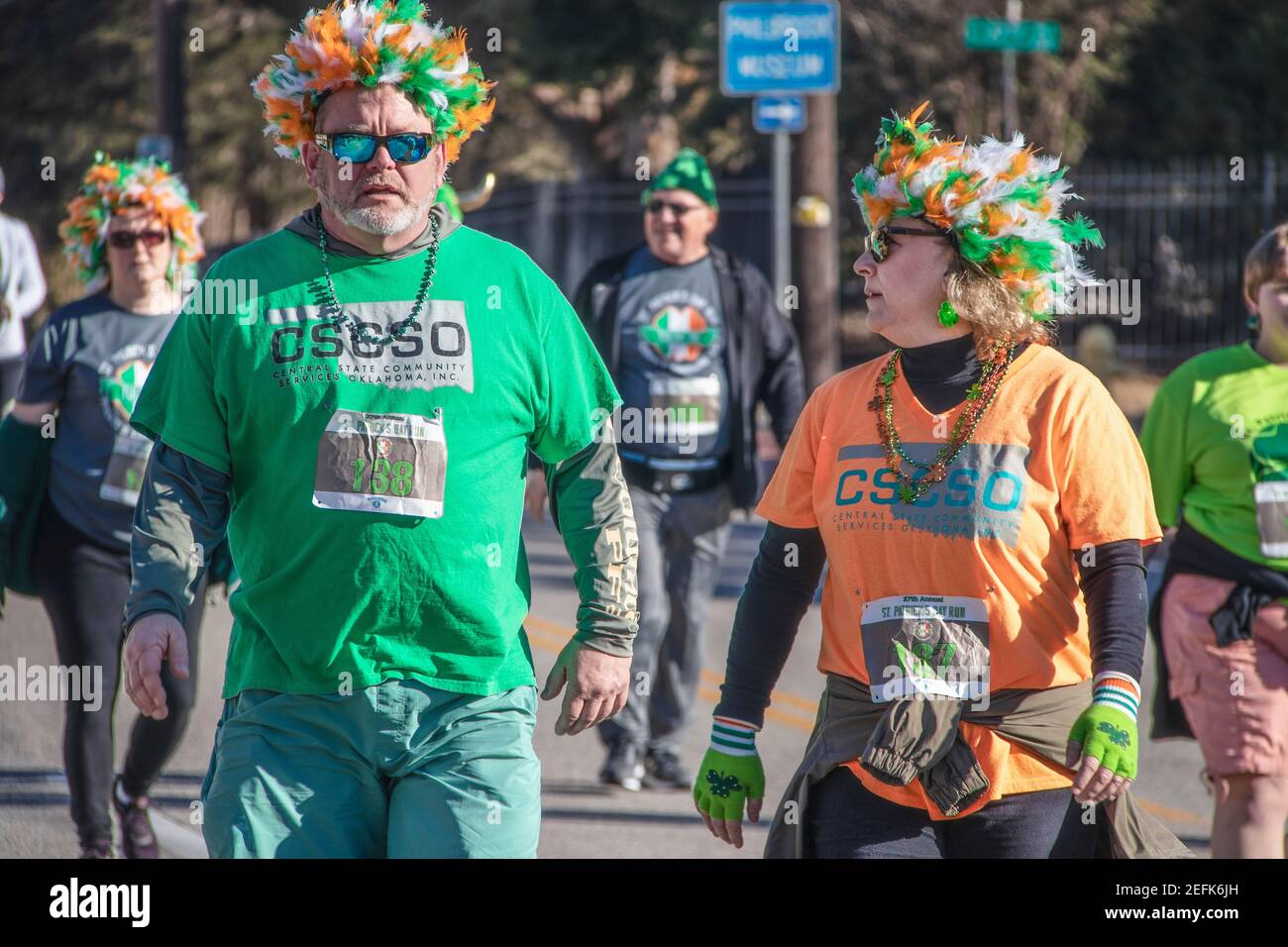 3-16-2019 Tulsa USA - Mann und Frau mittleren Alters Mit Federperücken und OCSO Teeshirts spazieren und plaudern St. Patricks Day Parade auf der Peoria Ave i Stockfoto