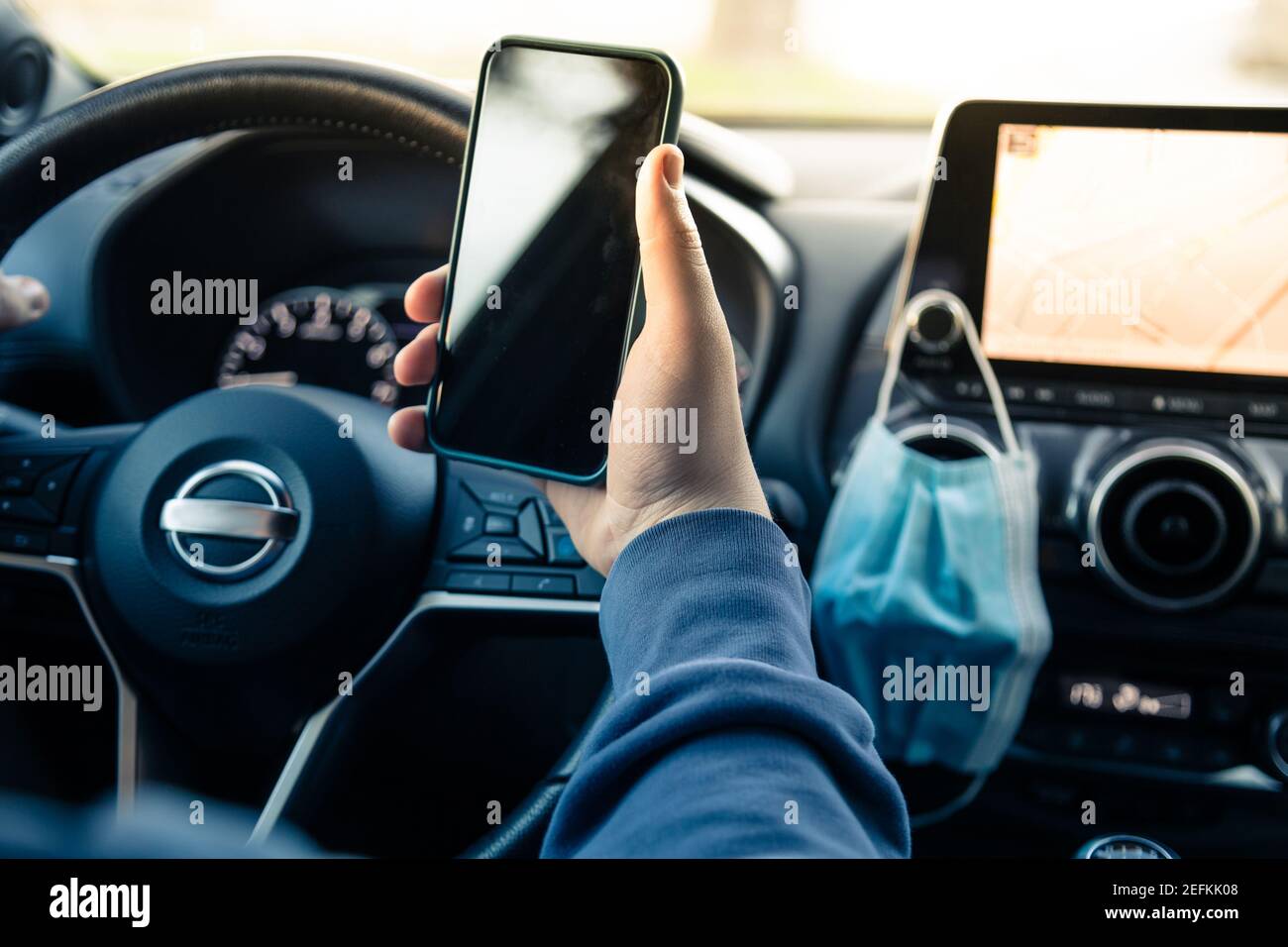 Teen fahren ein Auto und verwenden Smartphone. Junger Mann beim Lesen von Nachrichten mit einem Handy während der Fahrt. Gefährliches Verhalten, Unfallgefahr. Gefahr Stockfoto