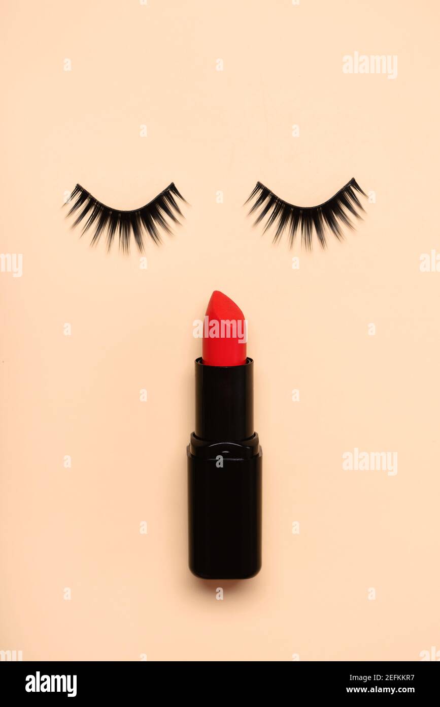 Falsche Wimpern und roter Lippenstift auf einem beigen Hintergrund.Schönheit und Make-up-Konzept Stockfoto