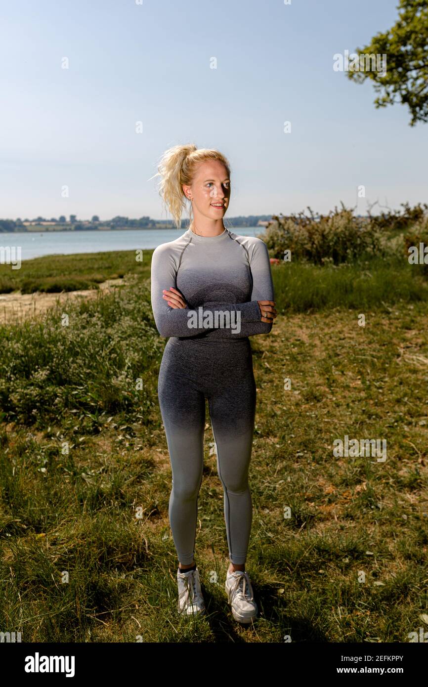 Attraktive Passform junge Frau in Sportkleidung bereit, in der Sonne am Flussufer zu trainieren. Gesundes Lifestyle-Konzept Stockfoto