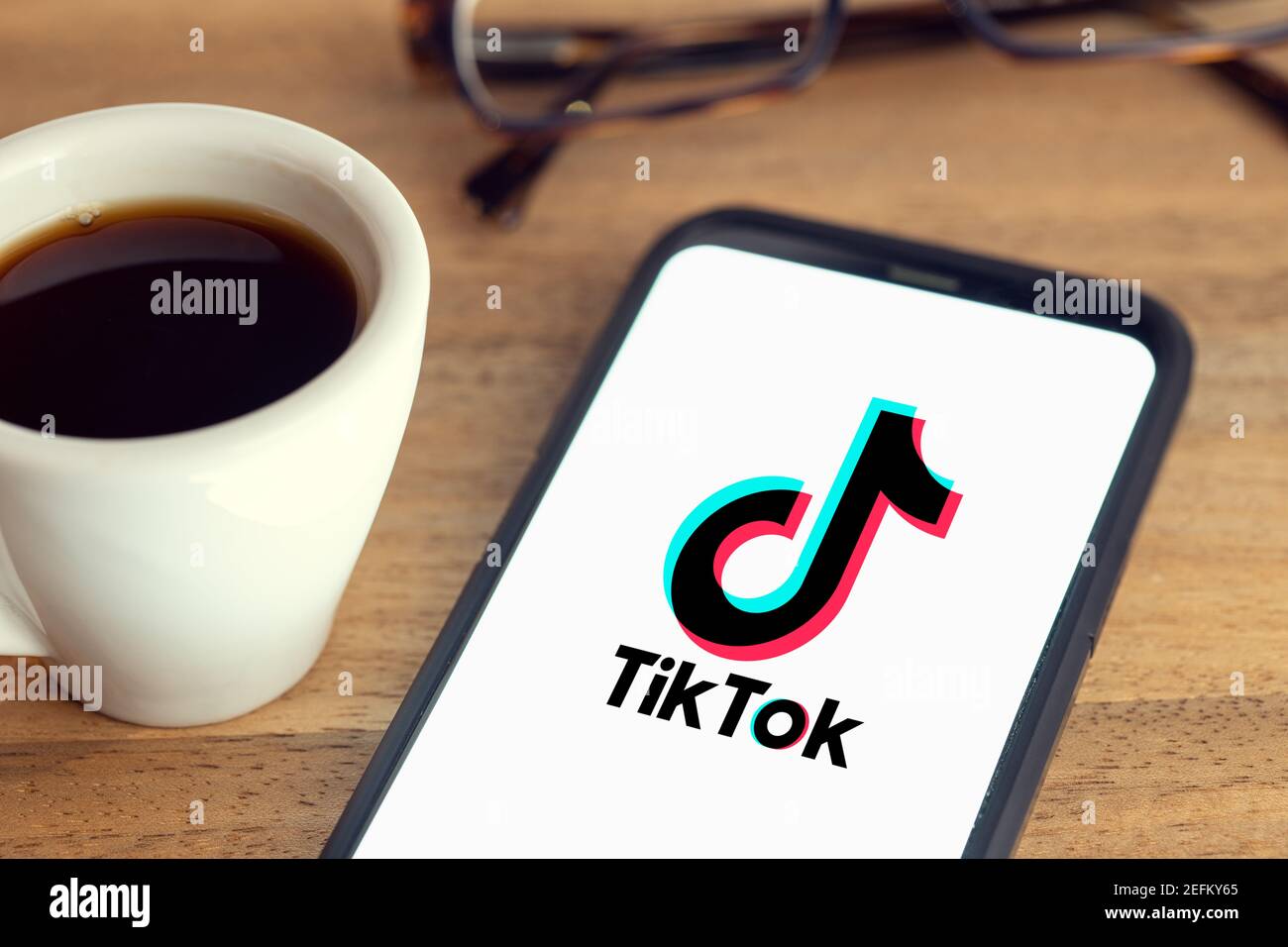 Galicia, Spanien; 15. februar 2021: TIK Tok Logo auf Smartphone-Bildschirm auf Schreibtisch mit Brille und Tasse Kaffee auf Holztisch Stockfoto