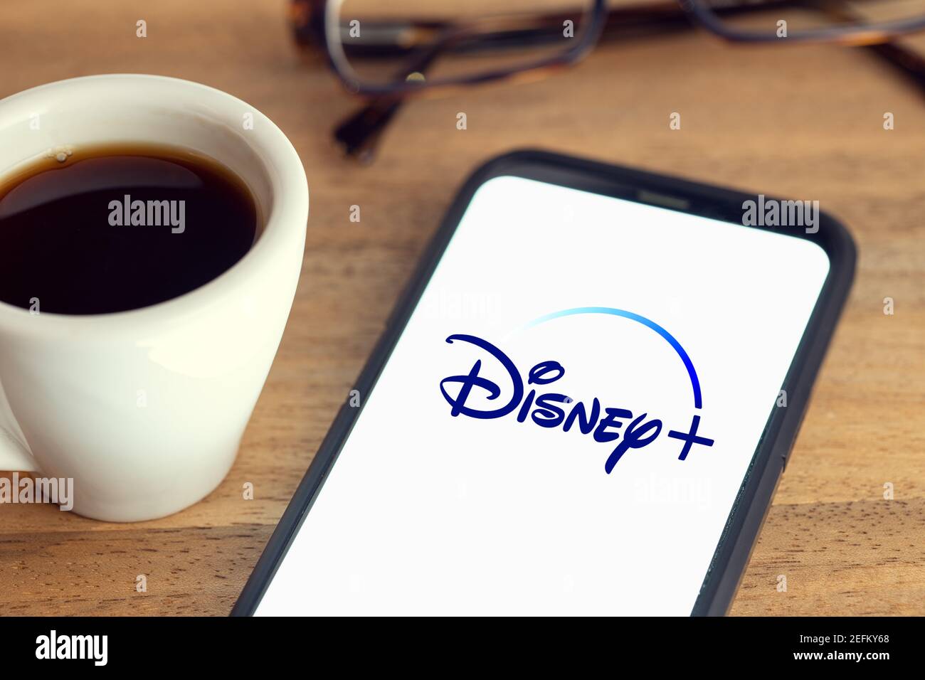 Galicia, Spanien; 15. februar 2021: Disney plus Logo auf Smart Phone Bildschirm auf Schreibtisch mit Brille und Tasse Kaffee auf Holztisch Stockfoto