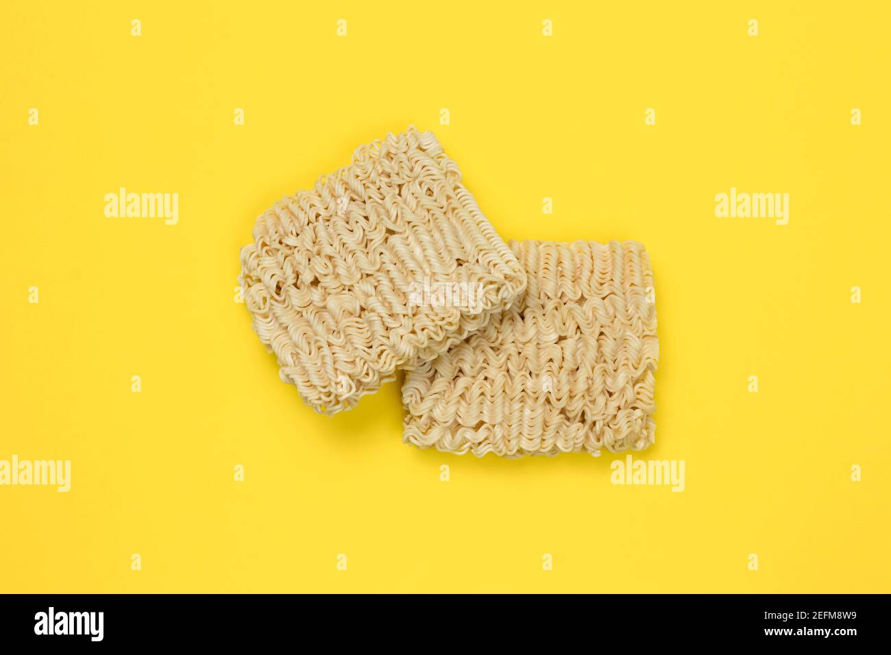 Instant Nudeln, Ramen, getrocknete Nudelblöcke auf gelbem Hintergrund. Ungesunde Ernährung Konzept. Ungekochte Pasta. Draufsicht. Traditionelle japanische Küche Stockfoto