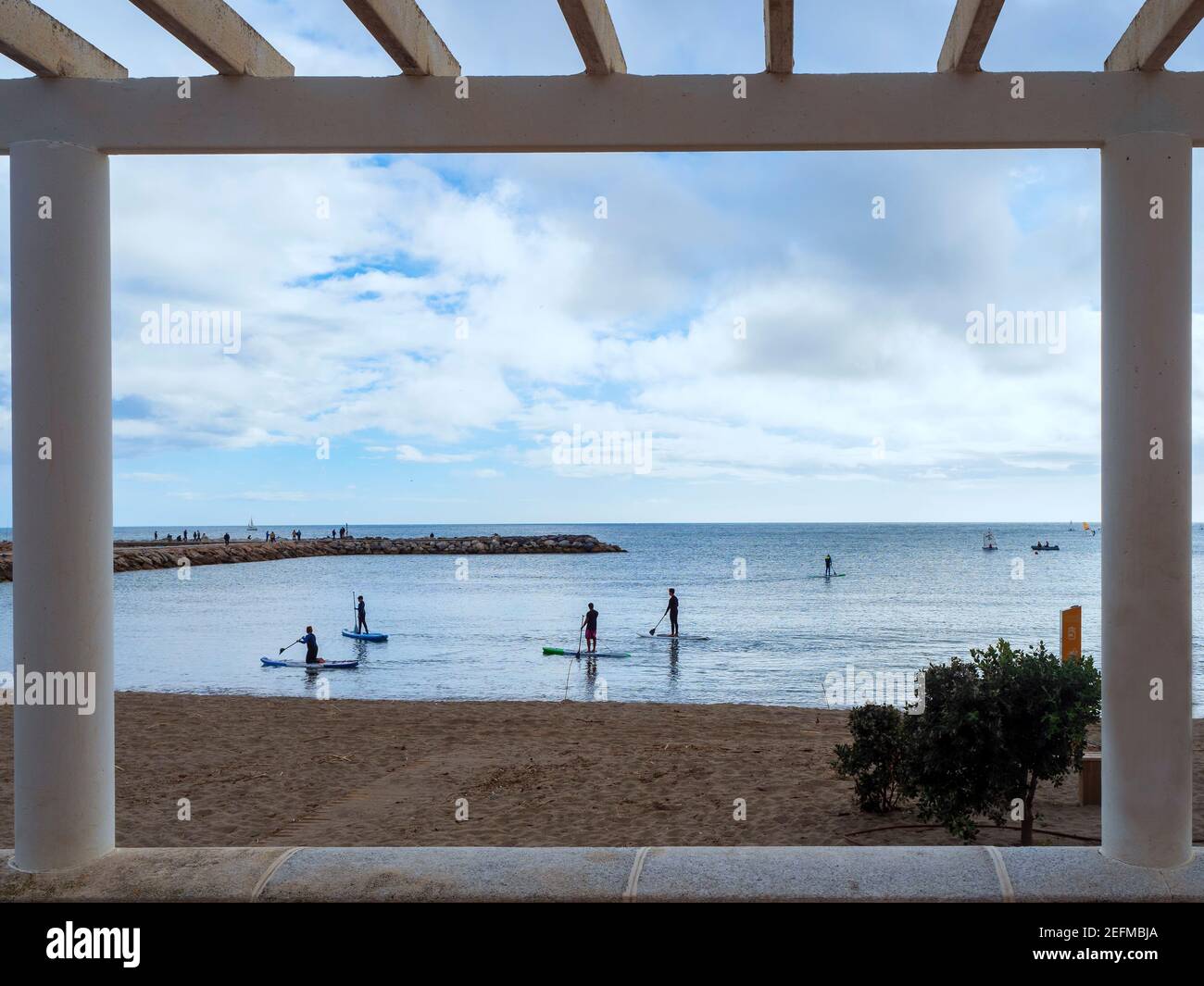 Blick von einer Pergola auf die Strandpromenade von einigen Surfer üben ihren Lieblingssport in den Gewässern der Hafen von Fuengirola an einem bewölkten Tag Stockfoto