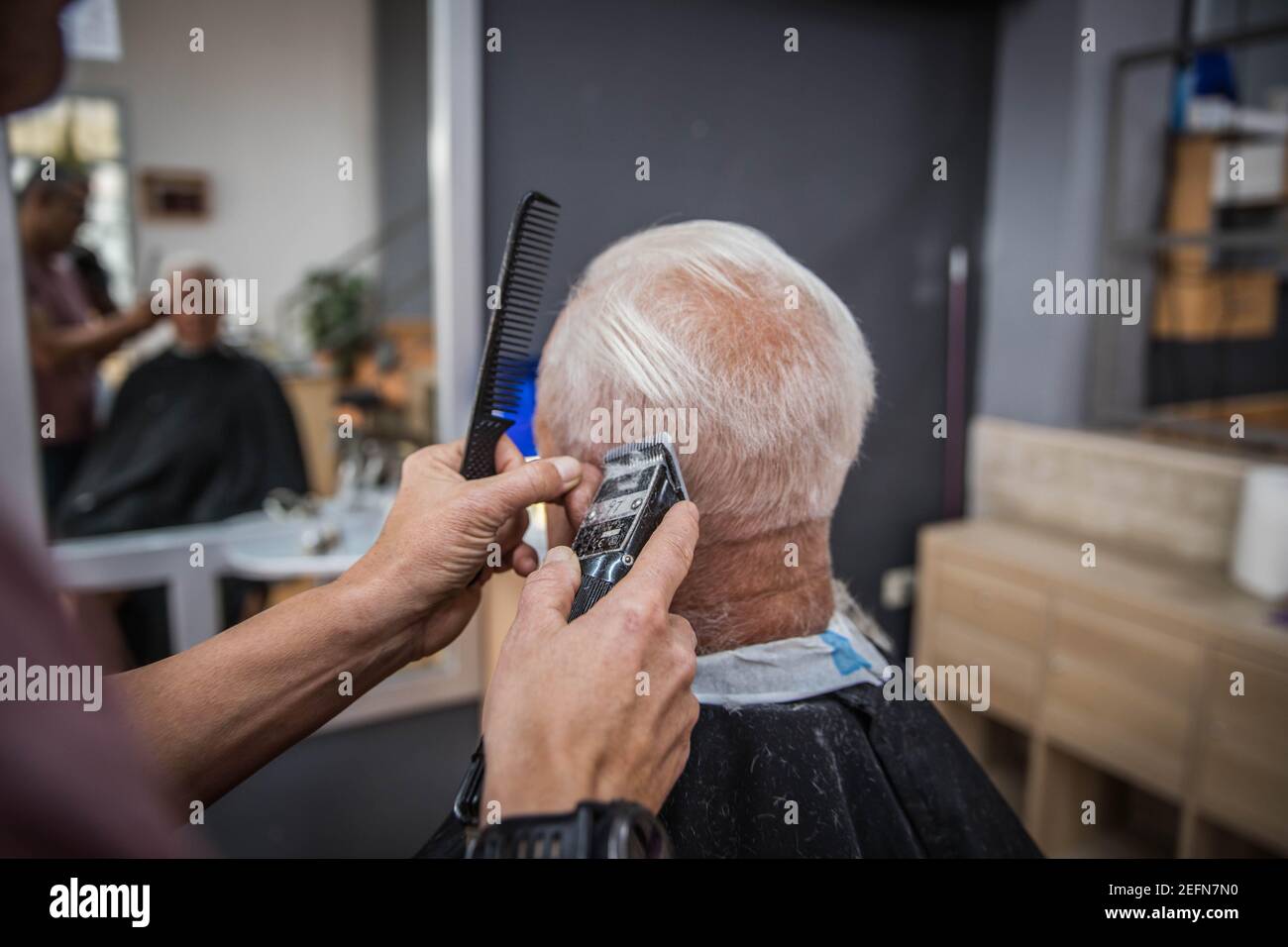 Barbier schneidet einem alten Kunden, einem herrn mit weißen Haaren, in seinem Friseurhaus Haare Stockfoto