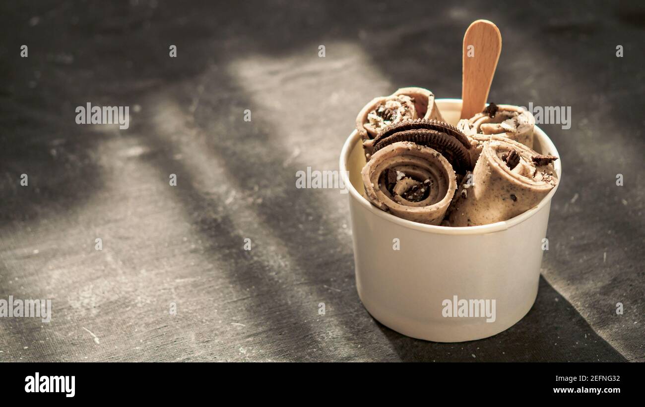 Gerollt Eis mit in Kegel Cup auf dunklen rustikalen Hintergrund. Iced Brötchen mit Gebäck Schokolade sandwich Cookies. Im thailändischen Stil gerollt Eis mit Kopie Platz für Text oder Design. Banner. Hartes Licht Stockfoto