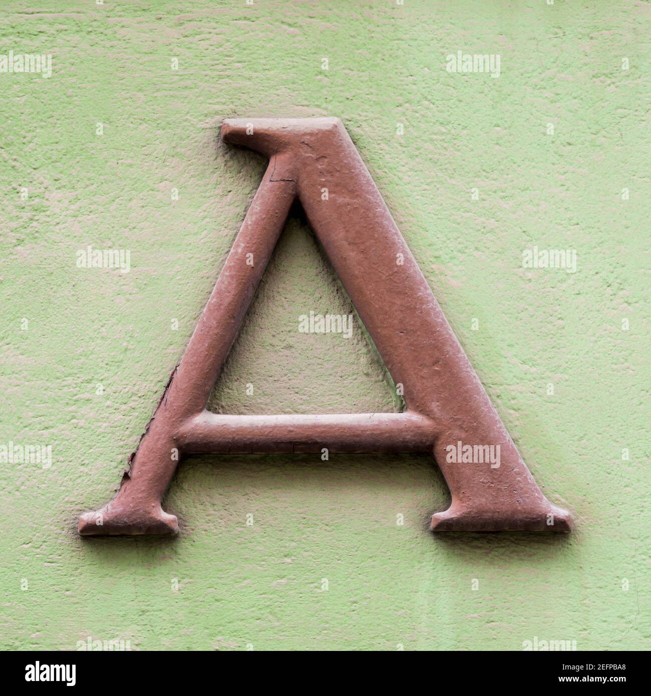 Brauner Buchstabe A mit Serifen auf grüner Hauswand Stockfoto