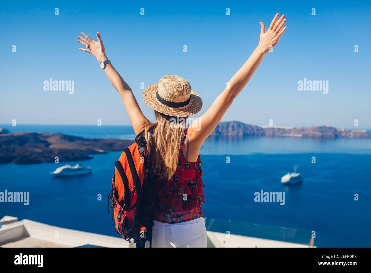 Glückliche Frau Reisende zu Fuß heben die Hände in Thera, Santorini Insel, Griechenland genießen Meereslandschaft und Kreuzfahrtschiffe. Sommerurlaub Stockfoto