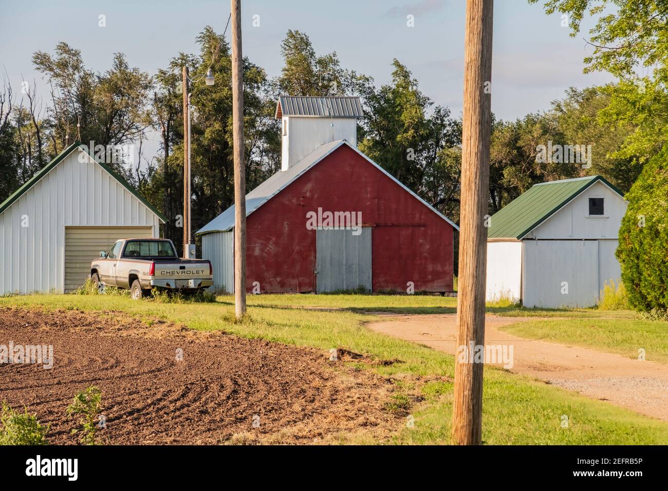 Ein Hof mit gepflügten Feld, eine rote Scheune und Nebengebäude. Kansas, USA Stockfoto