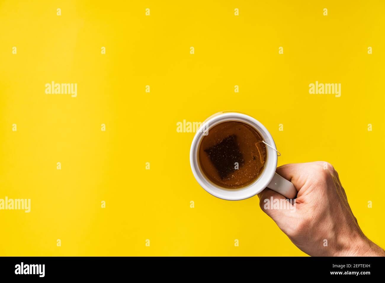 Draufsicht auf die Hände, die eine Tasse Tee vor sich halten Mit gelbem Hintergrund Stockfoto