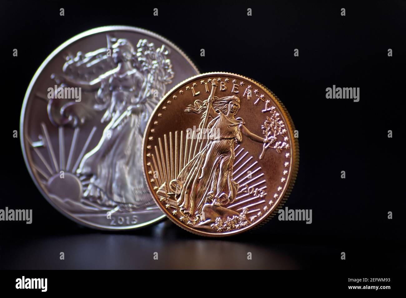 Eine im Fokus eine Unze Goldmünze mit einer Out of Focus American Silver Eagle Münze dahinter, auf einem schwarzen Hintergrund Stockfoto