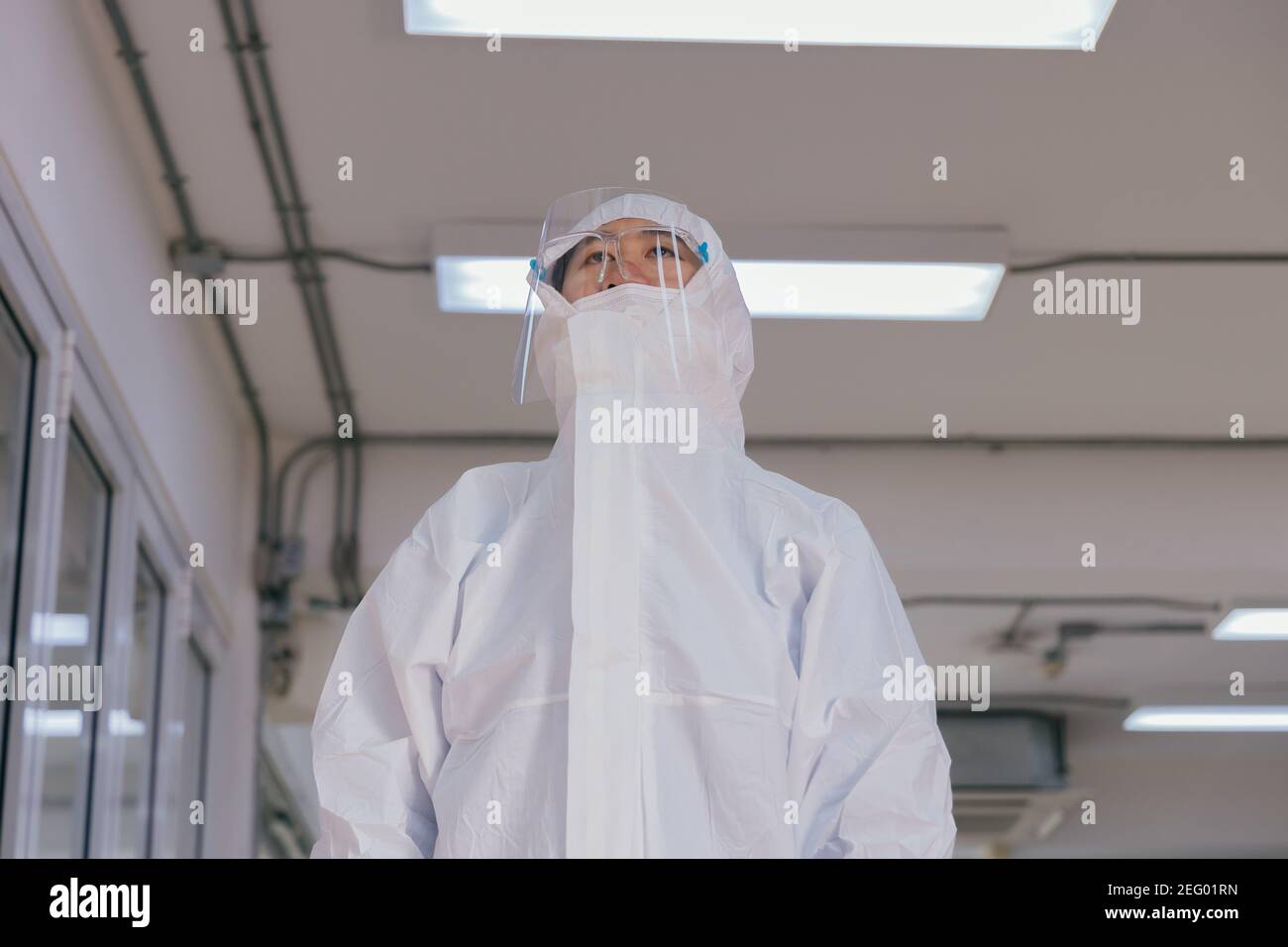 Müde junge medizinische Mitarbeiter tragen PSA-Anzug mit schützendem Gesicht Schild und Maske arbeiten im Krankenhaus während Covid-19 Pandemie Stockfoto