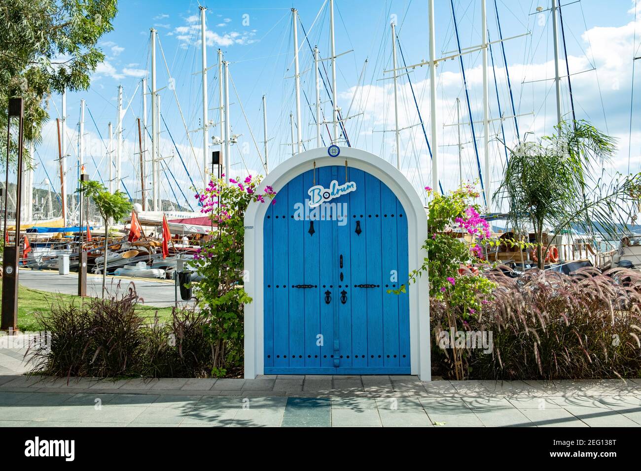 Symbolische blaue Tür mit dem Namen der Stadt Bodrum, Segelmasten und Bougainvillea Blume auf blauem Himmel Hintergrund an sonnigen Tag in Bodrum, Türkei. Stockfoto