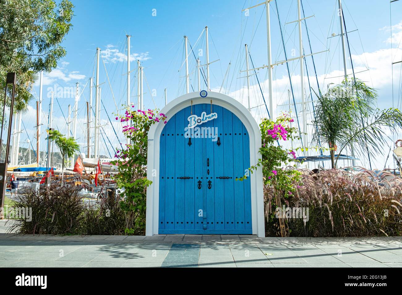 Symbolische blaue Tür mit dem Namen der Stadt Bodrum, Segelmasten und Bougainvillea Blume auf blauem Himmel Hintergrund an sonnigen Tag in Bodrum, Türkei. Stockfoto