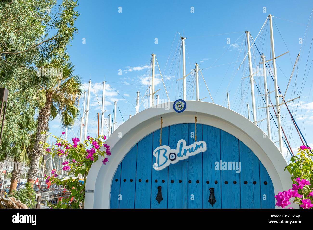 Symbolische blaue Tür mit dem Namen der Stadt Bodrum, Segelmasten und Bougainvillea Blume auf blauem Himmel Hintergrund an sonnigen Tag in Bodrum, Türkei. Stockfoto