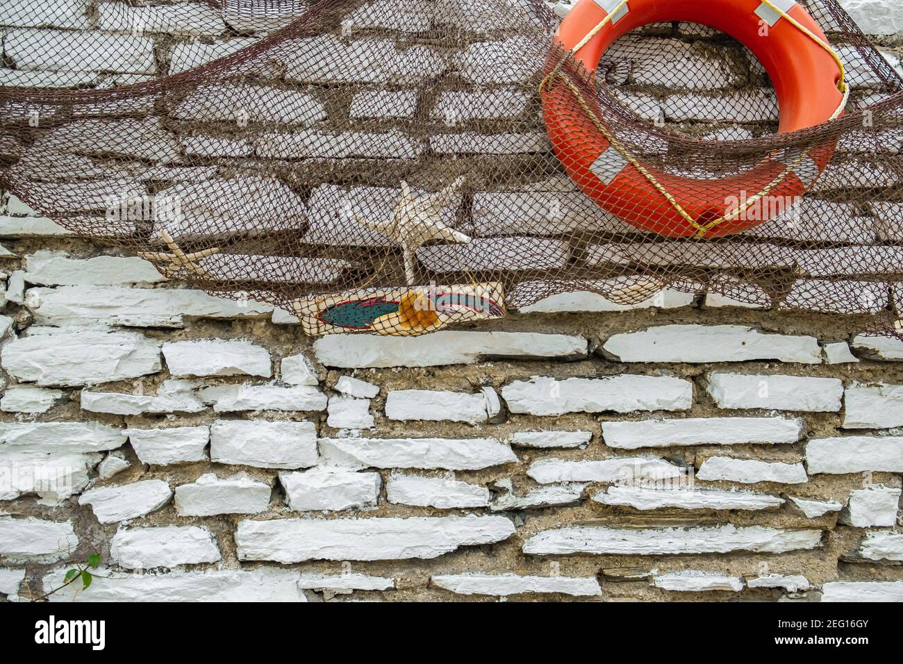 Weiße Backsteinmauer mit Fischernetzen, Zierfischen, Seesternen und orangefarbener Rettungsboje in einem Fischrestaurant. Stockfoto