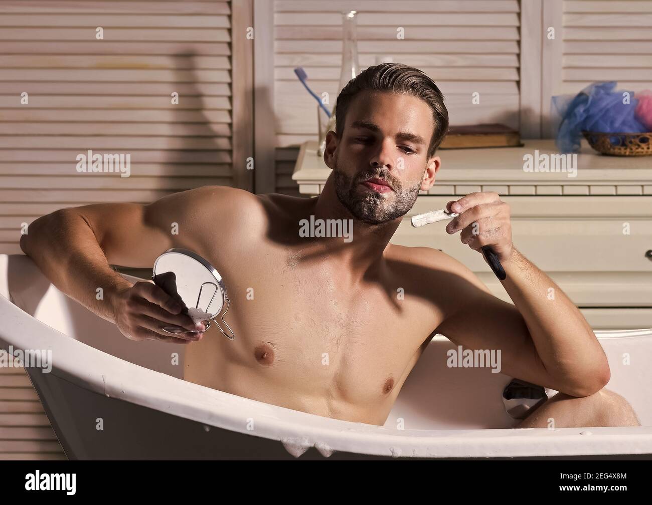 Junge attraktive Mann rasiert im Spiegel, Gay Rasieren im Bademantel im  Badezimmer Stockfotografie - Alamy