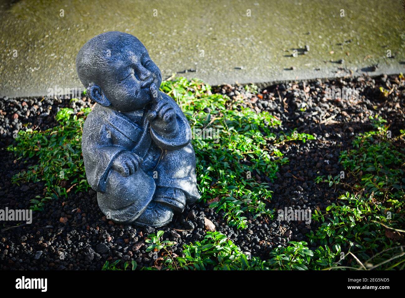 Stein buddhistische Mönchsstatue in einem Garten mit Handbewegung, um den Mund zu schließen. Drei Affen Konzept Stockfoto