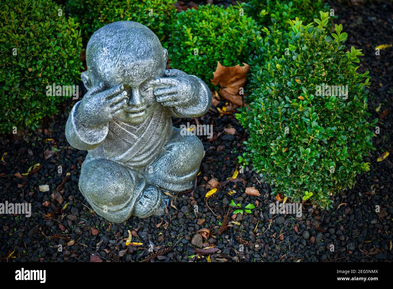 Stein buddhistische Mönchsstatue in einem Garten mit Handbewegung, um die Augen zu schließen. Drei Affen Konzept Stockfoto