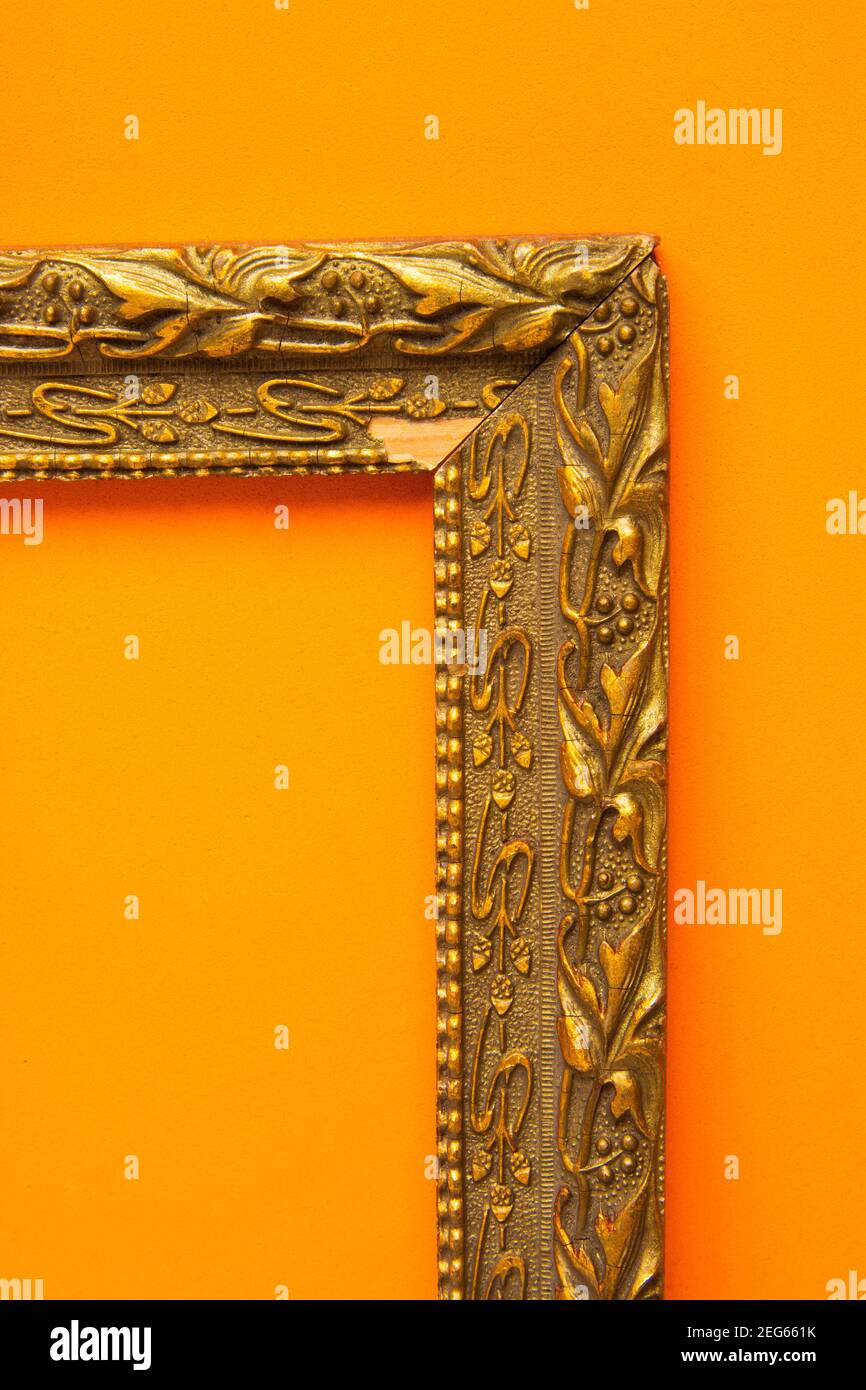 Dekorativer goldener Rahmen vor leuchtend orangefarbener Wand, der künstlerische Eleganz in der Innenarchitektur unterstreicht Stockfoto