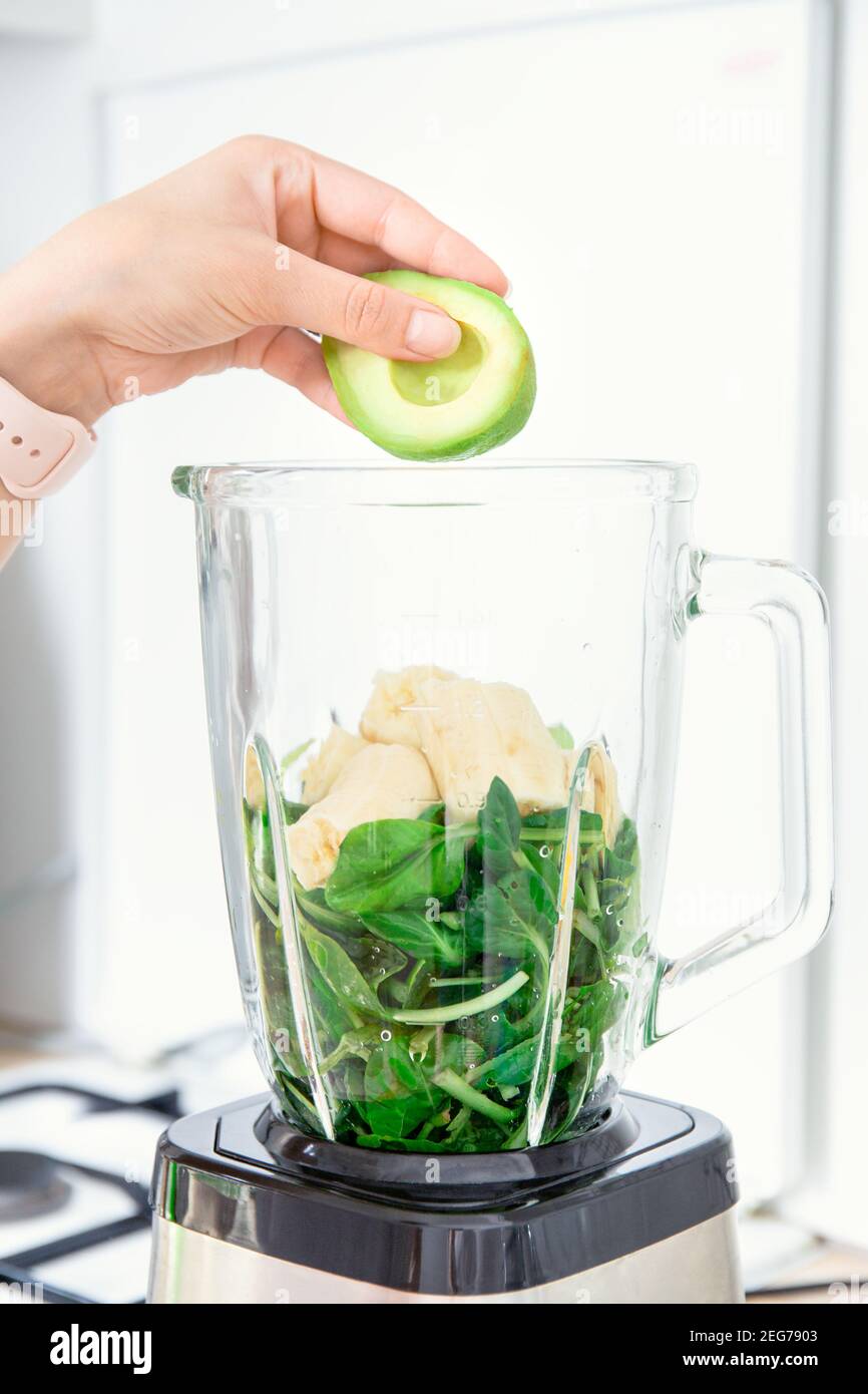 Zutaten für grüne Detox-Smoothies im Mixer. Spinat, Banane und Avocado. Seitenansicht. Hand füllt einen Mixer oder Mixer mit gesunden Zutaten: av Stockfoto