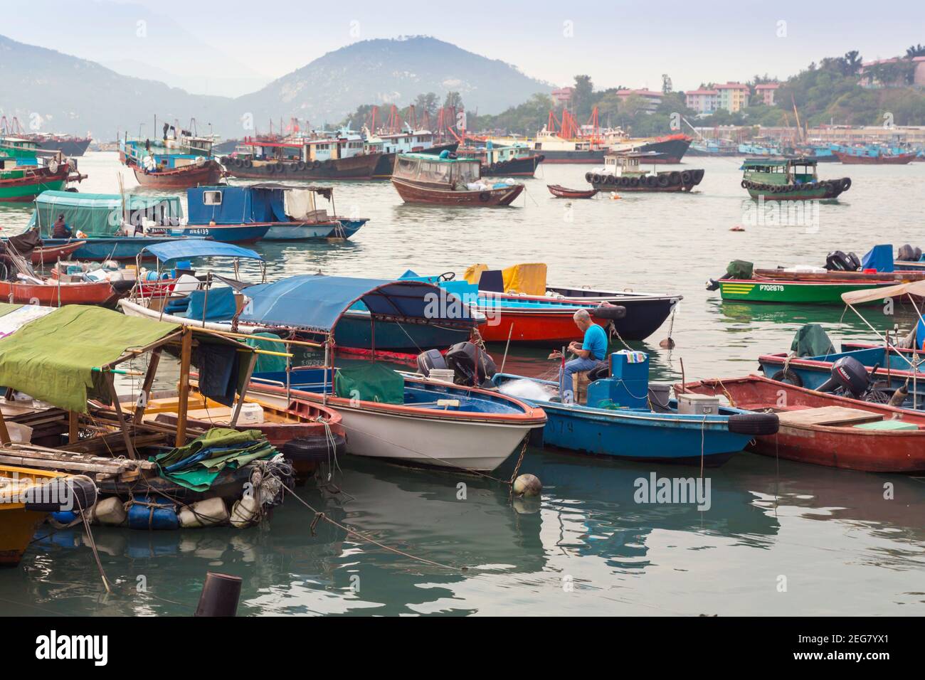 Cheung Chau Insel in der Nähe von Hong Kong, China. Der Hafen. Mann, der im Fischerboot sitzt, um Netze auszubessern. Stockfoto